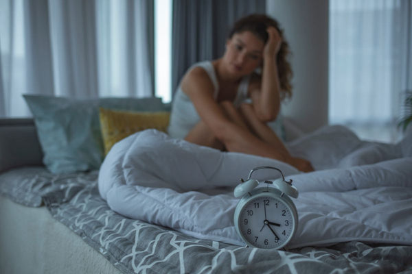 Mulher preocupada sentada na cama com despertador